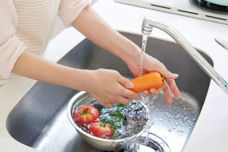 A woman washing vegetables in her kitchen sink. Call Michael Bonsby for all your plumbing needs