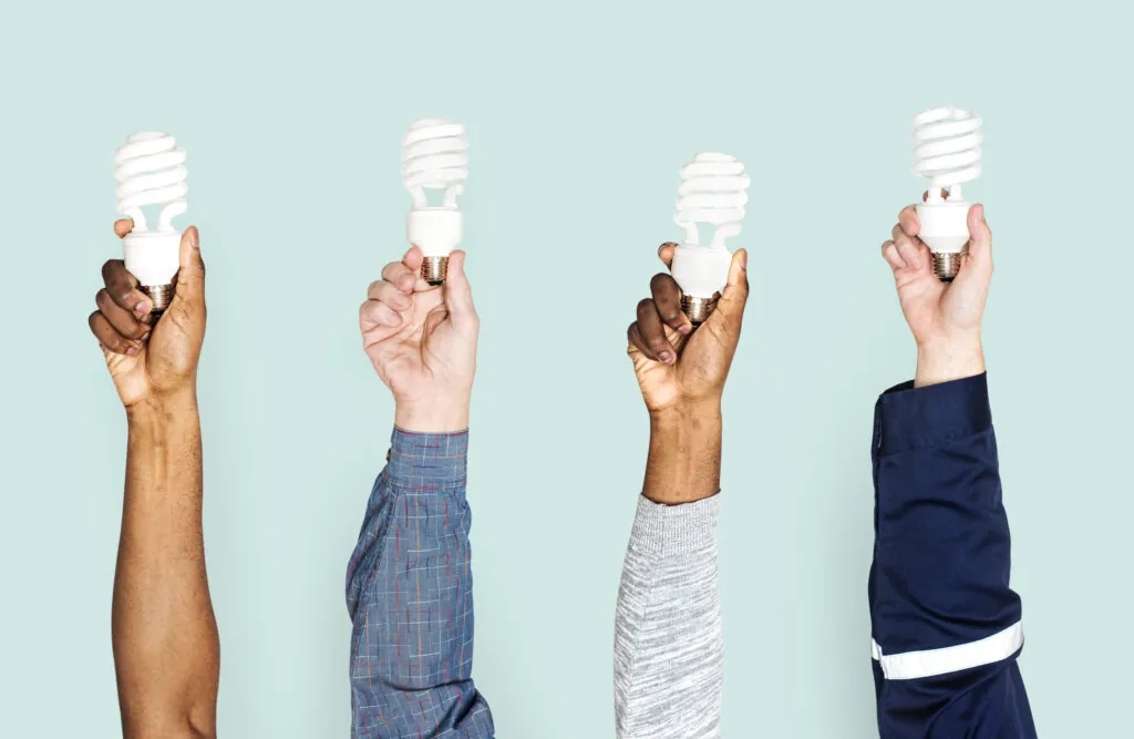 Four people's arms holding up different light bulbs. Light blue/teal background. Michael Bonsby HVAC in MD, VA, & DC