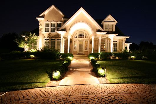 Exterior lighting installed in front of a large two-story home, lit up at night.